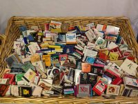 Wicker basket filled with hundreds of vintage matchboxes showing a mix of advertising and brand logos.