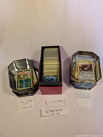 Full view of three tins and one box filled with Pokemon cards, with handwritten notes describing contents and dates