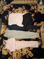 Overview of the five items including pink bra and leggings set, grey and blue pants, black shorts on floral carpet.