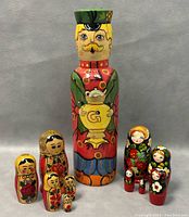 Front view of the painted lacquered wood bottle holder with samovar design and the two sets of Russian nesting dolls.