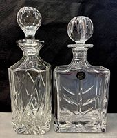 Two vintage crystal decanters side by side on black background showing different cut-glass designs and stoppers