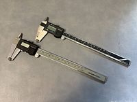 Two Mitutoyo Digimatic digital calipers side by side on grey surface