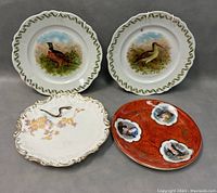 Four plates shown together on gray background: two Royal Austrian collectible plates with bird designs, one white plate with snake and floral motif, one red plate with images of women.
