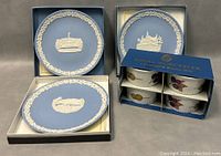 Three blue Wedgwood Jasperware collector plates with white relief architectural designs and decorative border, displayed in original boxes alongside a blue box containing three Royal Worcester Evesham ramekins with fruit decoration.