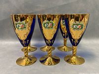 Photo of six gold and cobalt blue vintage wine glasses showing their front sides with hand painted floral designs and twisted stems.