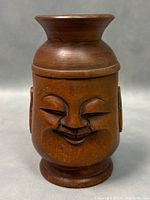 Front view of wooden humidor box showing stylized smiling face carving and lid on.