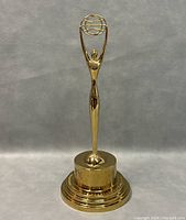 Front view of 14 inch tall gold Clio Award trophy with stylized figure and circular design above head.