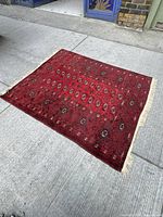 Full view of the red handwoven rug laid out on concrete, showing pattern and dimensions.