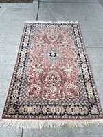 Top-down view of rectangular handwoven rug with floral medallion pattern and fringed ends on a concrete floor.