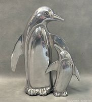 Front view of polished metal penguin with chick figurine showing reflective surfaces and detailing