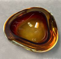 Top-down view of rounded triangular amber glass bowl showing gradient color and glossy finish, highlighting thickness and clarity of Murano Sommerso glass.