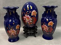 Photo showing pair of matching Chinese porcelain vases flanking a porcelain egg with floral design, all on neutral background.
