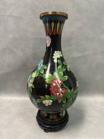 Full view front of the black cloisonné vase with floral patterns and brass rim, on wooden stand.