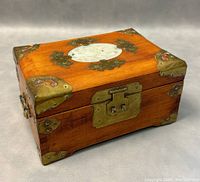 Angled view of the wooden jewelry box showing brass corner accents, brass latch, and ring handle on side.