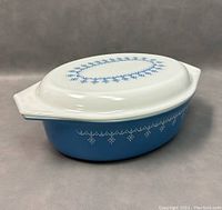 Side and top view of vintage Pyrex lidded casserole dish showing blue snowflake pattern on white lid and blue base.