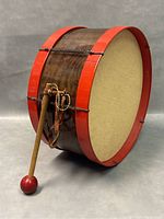 Side view of vintage toy drum with red rims, wooden body, and attached drumstick with string.