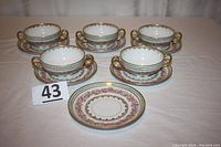 Five double-handle cups and six matching saucers arranged with one extra saucer in front. Each cup and saucer decorated with intricate flower patterns and gold accents.