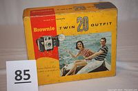 Original Kodak Brownie Twin 20 Outfit box with yellow, red, and black design showing a man and a woman on a boat, box is worn and taped on one side.
