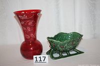 Photo showing red decorative vase with etched holly design and adjacent green ceramic Christmas sleigh holly berry design