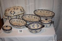 Photo showing all seven pieces including the large enameled metal roaster and six pottery serving pieces with blue and yellow floral design on cream background displayed on a white table.