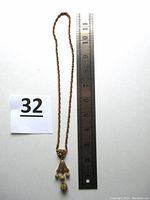 Full length view of the necklace laid flat next to a ruler showing total length of 19 inches, with ornate pendant details and chain visible
