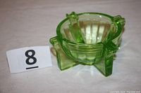 Side view of the green uranium vaseline glass ashtray highlighting ribbed bowl and four protrusions that serve as rests for cigarettes.