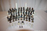 View of almost complete set of 36 painted plastic U.S. Presidents figurines arranged on white Styrofoam semi-circular display with two white columns.