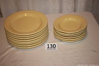 Full view of set of 8 yellow stoneware dinner plates and 6 scalloped shallow bowls stacked on table with lot number marker.