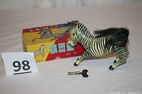 Photo showing the litho metal zebra toy alongside its colorful original box and the wind-up key placed in front.