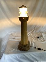 Front view of the lighthouse lamp illuminated showing its light on with inline switch and wooden base.