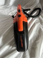 Top-down front angled shot showing black and orange Vacuum with two control buttons and coiled 12V power cord with car plug.