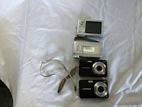 Five small digital cameras arranged on a white background, showing front and back views