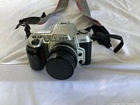 Front view of silver Nikon F60 film camera with lens cap attached and camera strap visible.