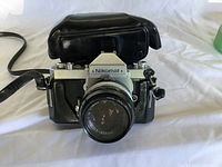 Front view of Nikon Nikomat camera with attached Nikkor lens on a white surface, showing camera body and lens condition.