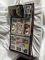 Open binder displaying pages of hockey cards in plastic sleeves, with a box of hockey cards on top.
