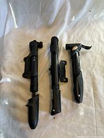 Photo showing three black handheld bicycle pumps with mounting brackets on a white fabric surface.