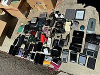 Overview of the collection on concrete floor showing phones, cameras, handheld devices, speakers, and chargers