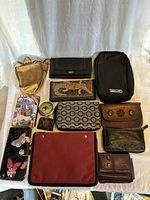 Box of various ladies purses and fashion accessories laid out on white cloth background in natural light showing variety, textures, and condition.