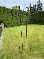 Two black metal garden stakes standing on grass, one taller with two hooks, one shorter with one hook, both with ground stakes for installation.