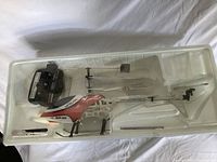 Remote control helicopter and radio controller placed in molded white plastic tray insert, helicopter white and red with flame decals, black rotors, controller black with two joysticks.