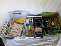 Three boxes filled with various craft and office supplies including scissors, rulers, paper clips, and stickers.