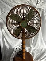 Front view of the Deco-Breeze oscillating fan showing the metal cage, four green blades, and wooden style stem and base.