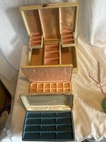 Photo showing open larger beige jewelry box with multiple pink and blue lined compartments
