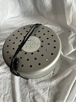 Round silver/gray metal marine dehumidifier with black power cord wrapped around, top surface features many circular holes for air flow.