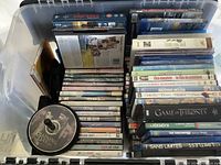 Overhead view of open plastic bin filled with about 100 DVDs in cases. Various genres and titles including Game of Thrones visible.