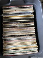 View of approximately 100 vinyl records stacked vertically inside a large container, showing wear and a variety of spine colors.