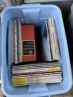 Top view photo of a blue plastic bin filled with approximately 60 vinyl records. Records stored both vertically and horizontally, includes a boxed edition titled 'The Columbia Encyclopedic Edition' and various other albums.