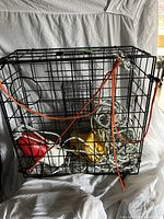 Photo showing black metal crab pot trap with orange ropes tied around and floats inside the trap.