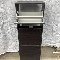 Storage unit front with the top compartment open showing white drop-down inner structure for organizing items.