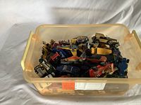 Plastic bin filled with approximately 20 assorted toy cars including Dinky Toys and Hot Wheels.